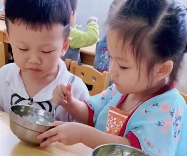 四川一幼儿园小男孩吃饭很慢，女孩主动给他喂饭，动作熟练又可爱